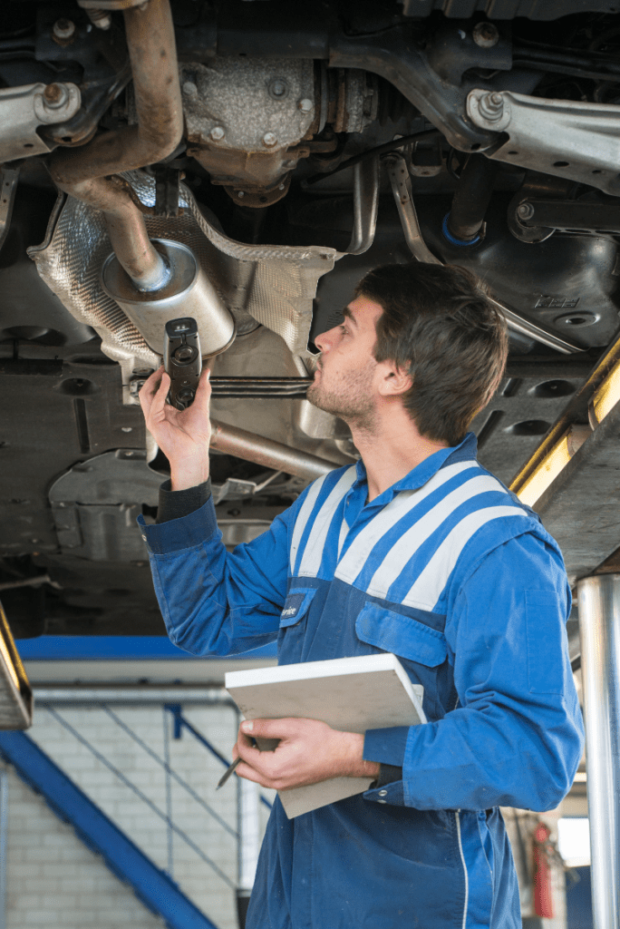 Mechanic in blue overalls underneath a vehicle during an inspection - car garage Raunds